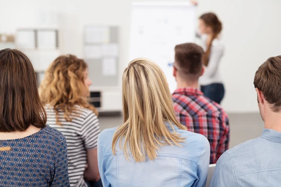 Salle de formation moderne avec groupe d'adultes assis face &agrave; une formatrice debout devant tableau blanc